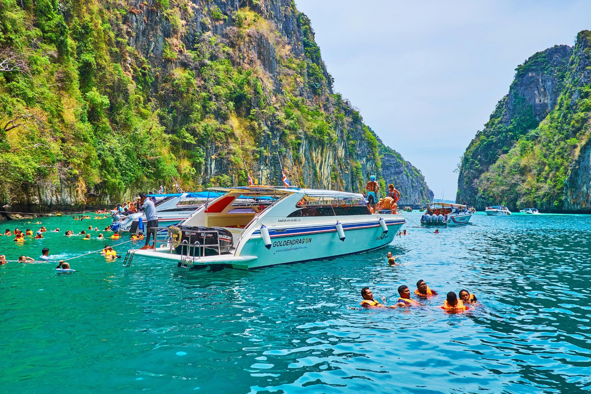 Tourists swimming near boats in Krabi's green water and cliffs
