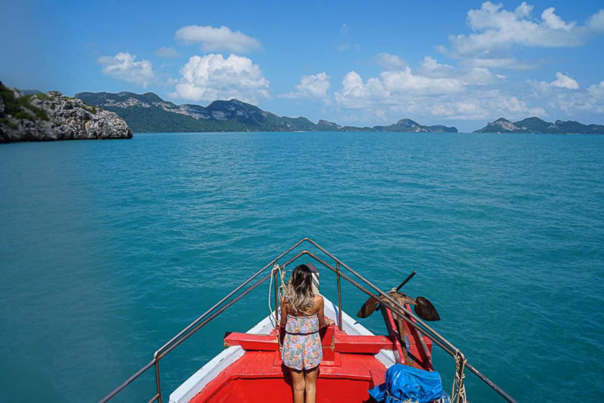 Woman on red boat heading toward green islands in Thailand
