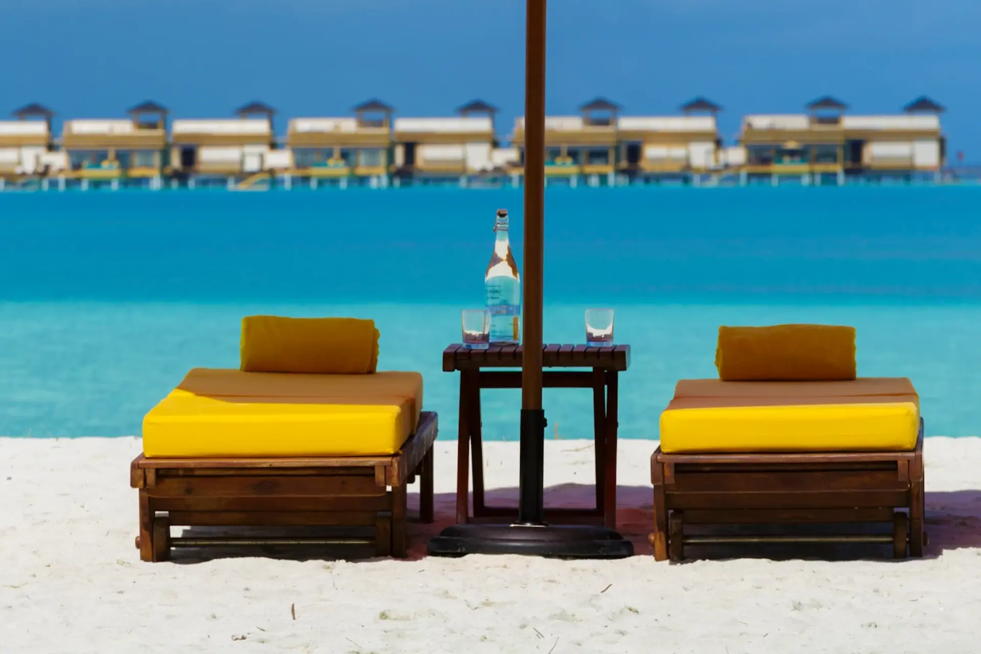 Two yellow loungers and small table facing blue water at Angsana Velavaru Resort