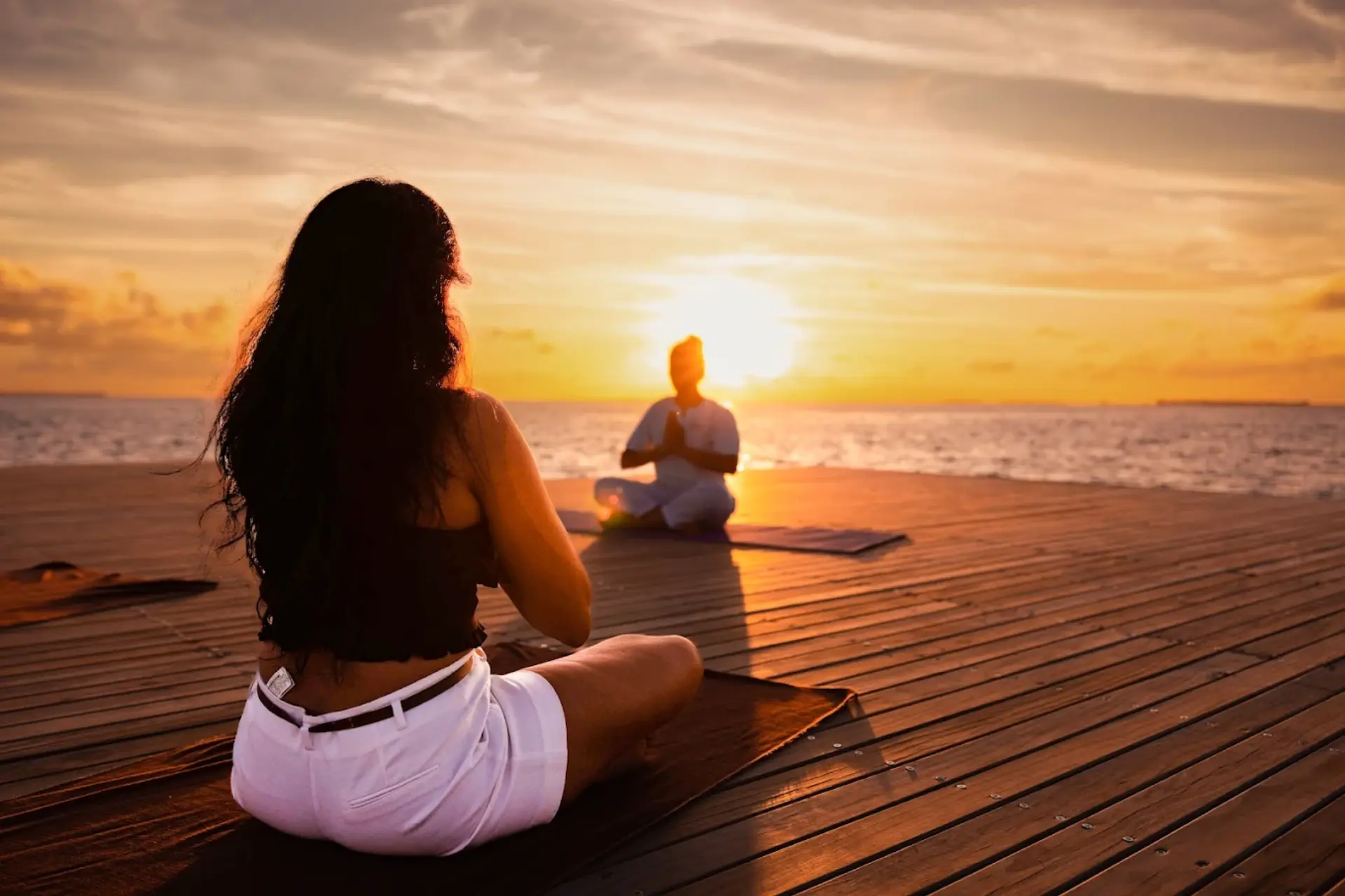 Two women doing yoga on wooden deck at Siyam World at sunset