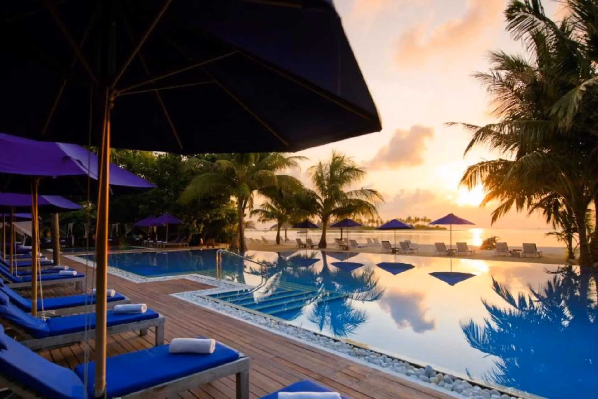 Sunset view of pool with blue umbrellas and ocean