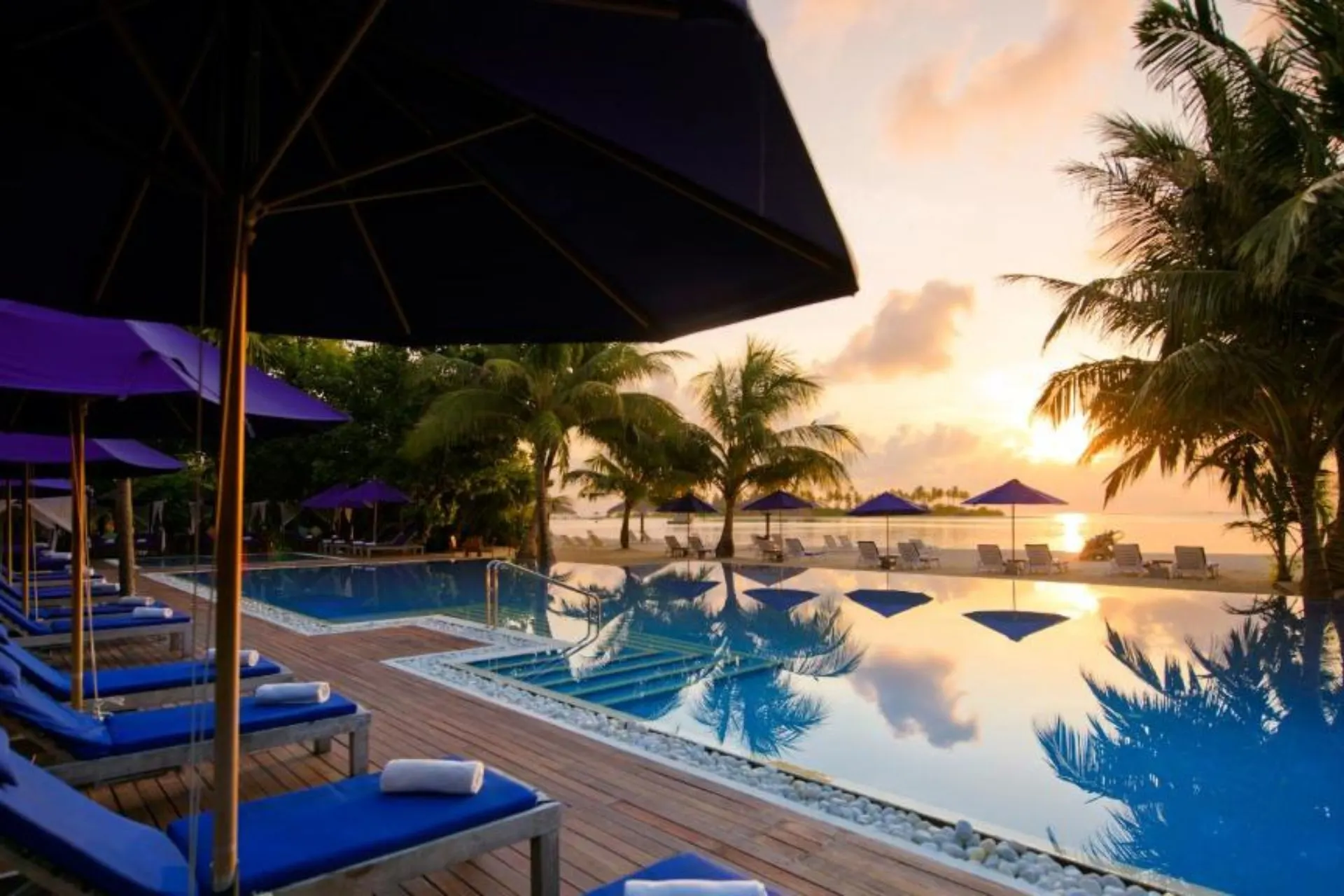 Sunset view of pool with blue umbrellas and ocean