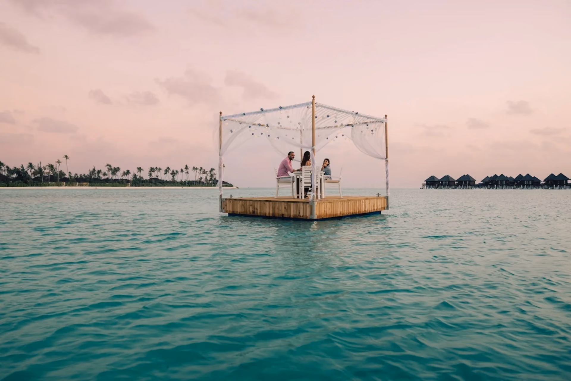 Couple dining in white canopy over blue-green water at Sun Siyam Resort