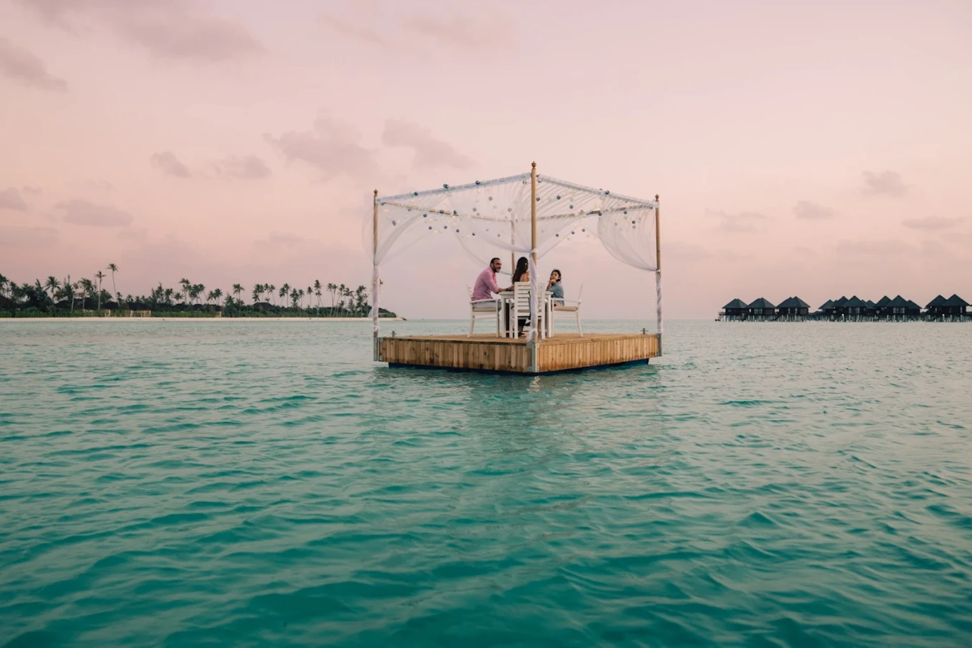 Couple dining in white canopy over blue-green water at Sun Siyam Resort