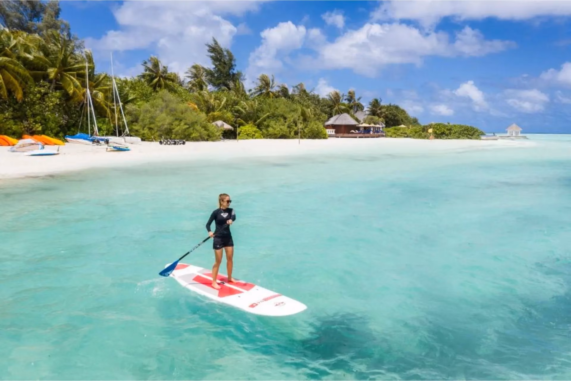 Child paddleboarding in clear blue-green water at tropical beach