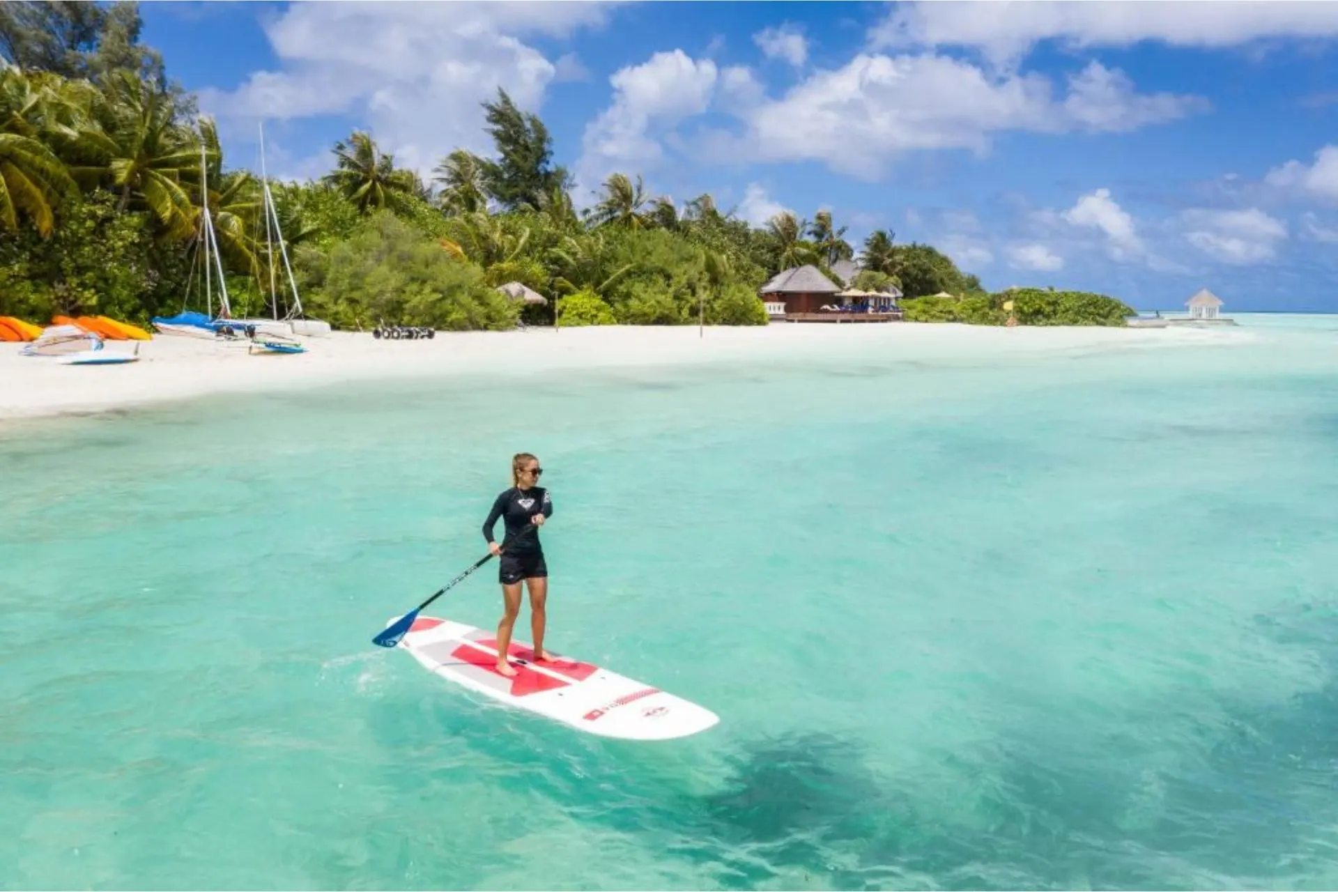 Child paddleboarding in clear blue-green water at tropical beach