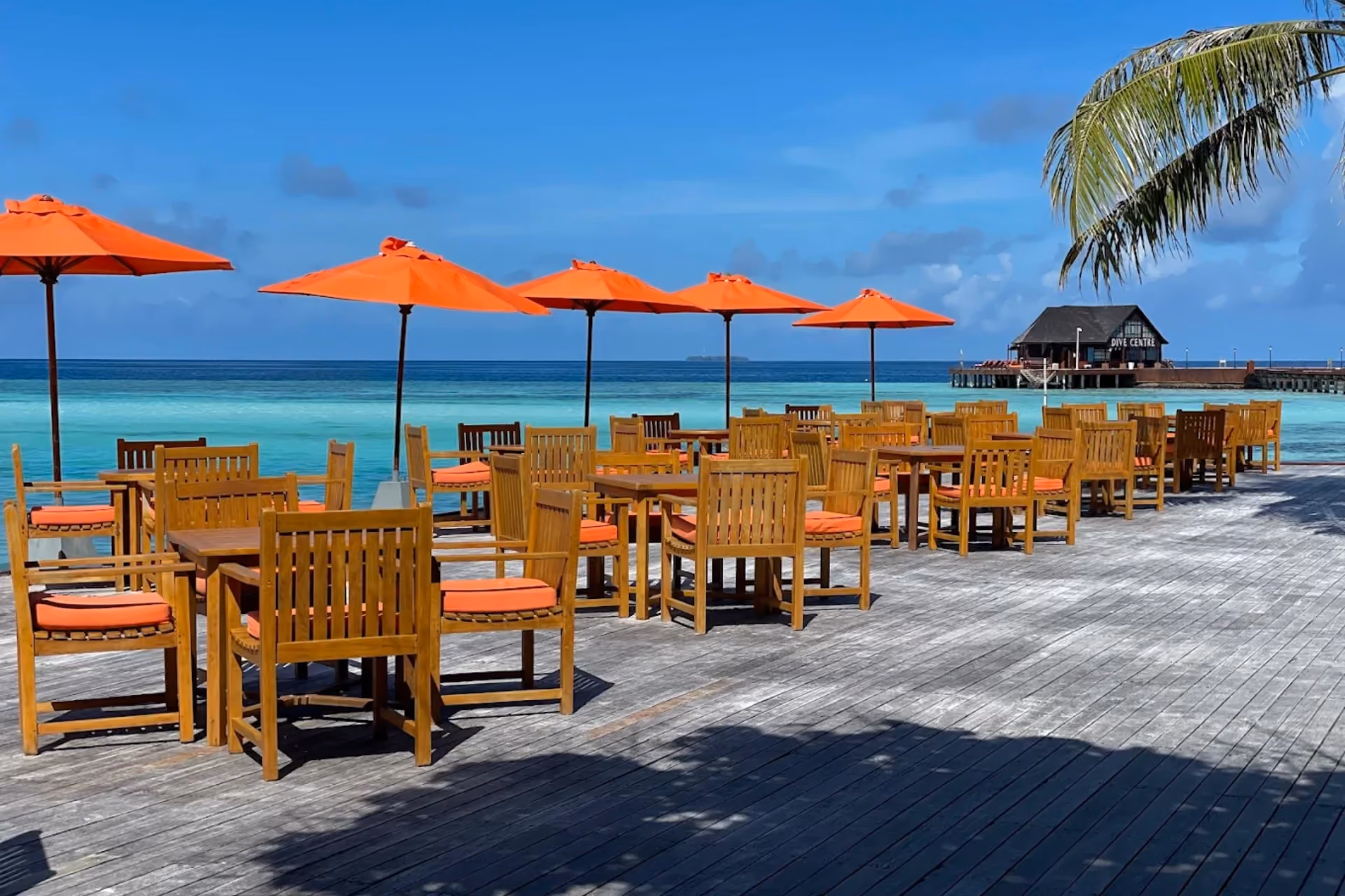 Sun Siyam Resort beach dining with orange umbrellas and wooden chairs