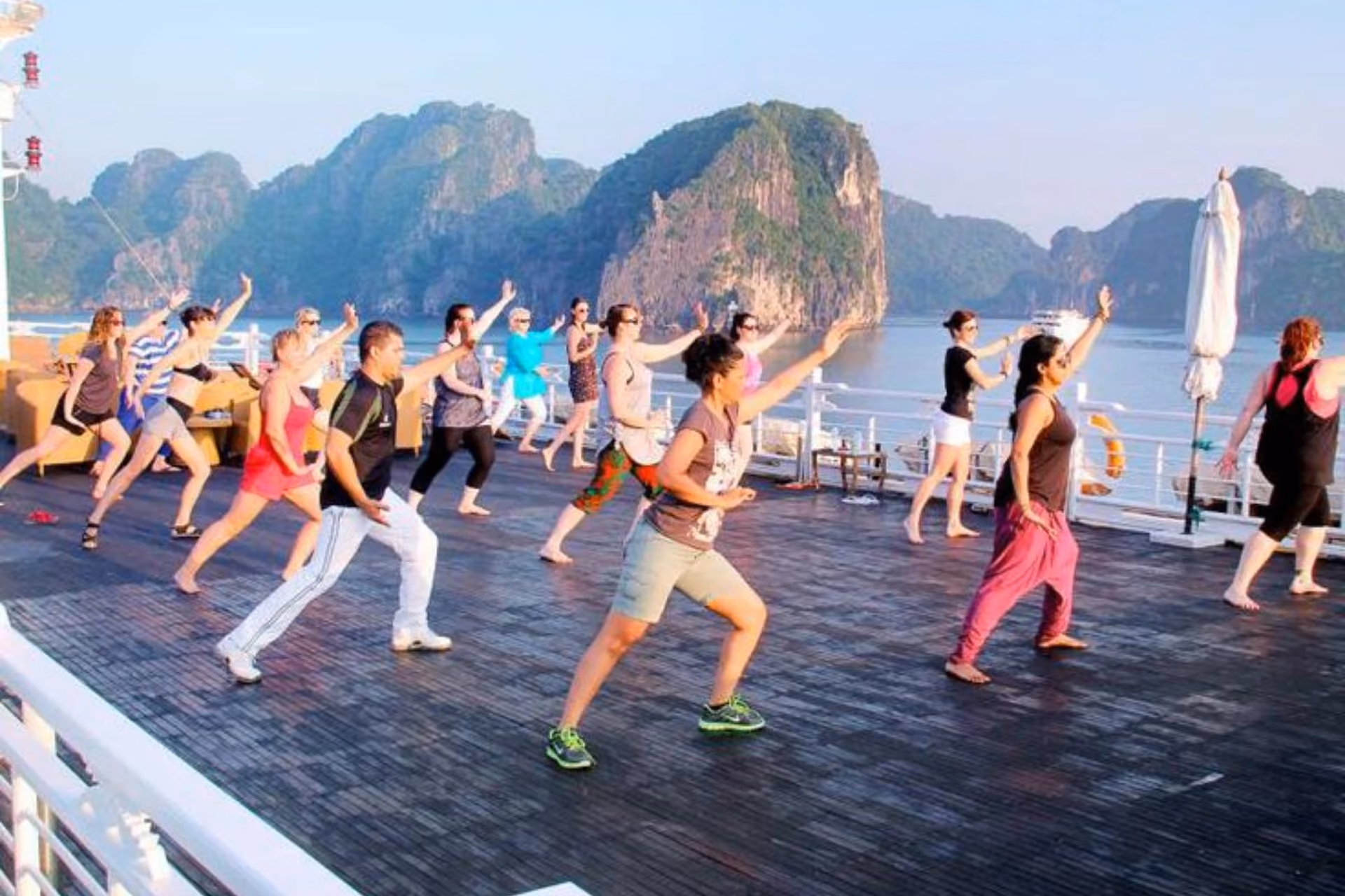 Group doing tai chi on boat deck near limestone islands