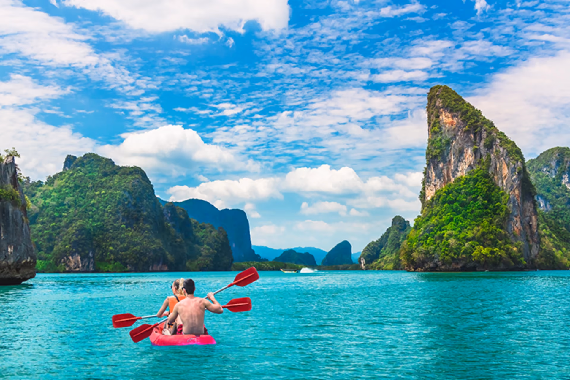 Two children kayaking in clear blue water near tall green cliffs