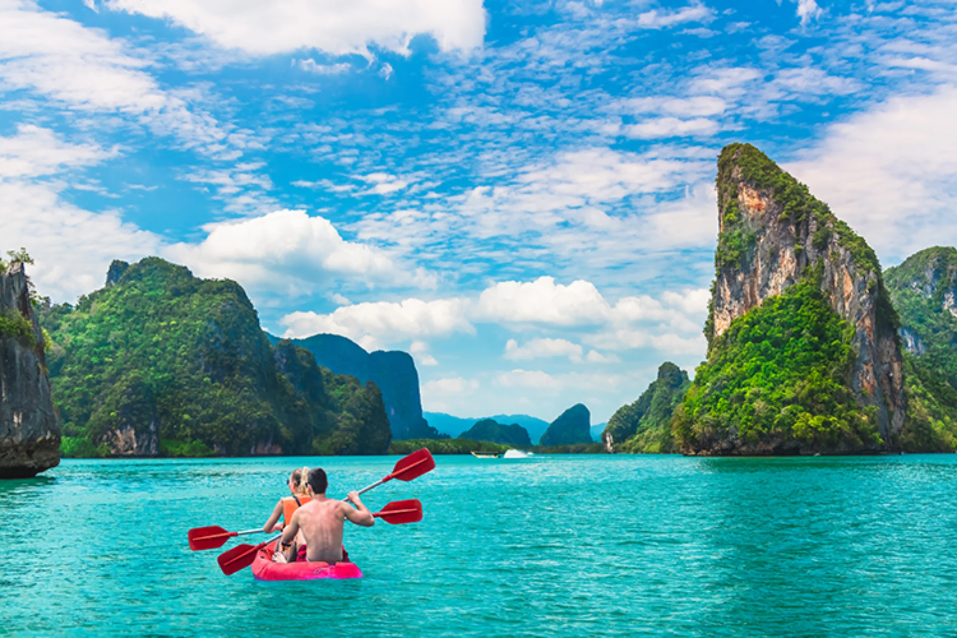 Two children kayaking in clear blue water near tall green cliffs