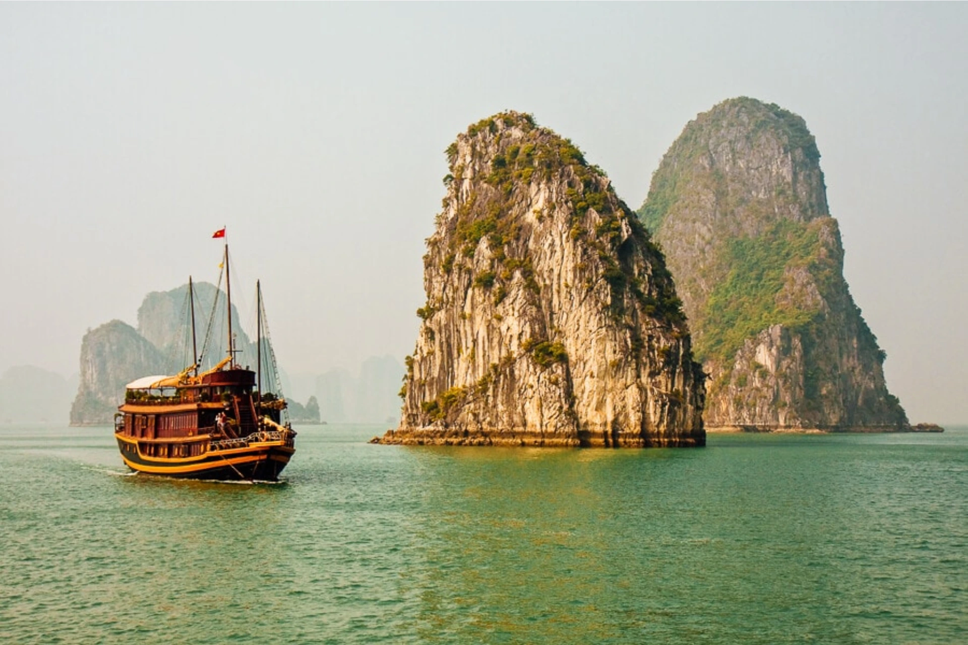 Traditional wooden boat near tall rock islands in Halong Bay