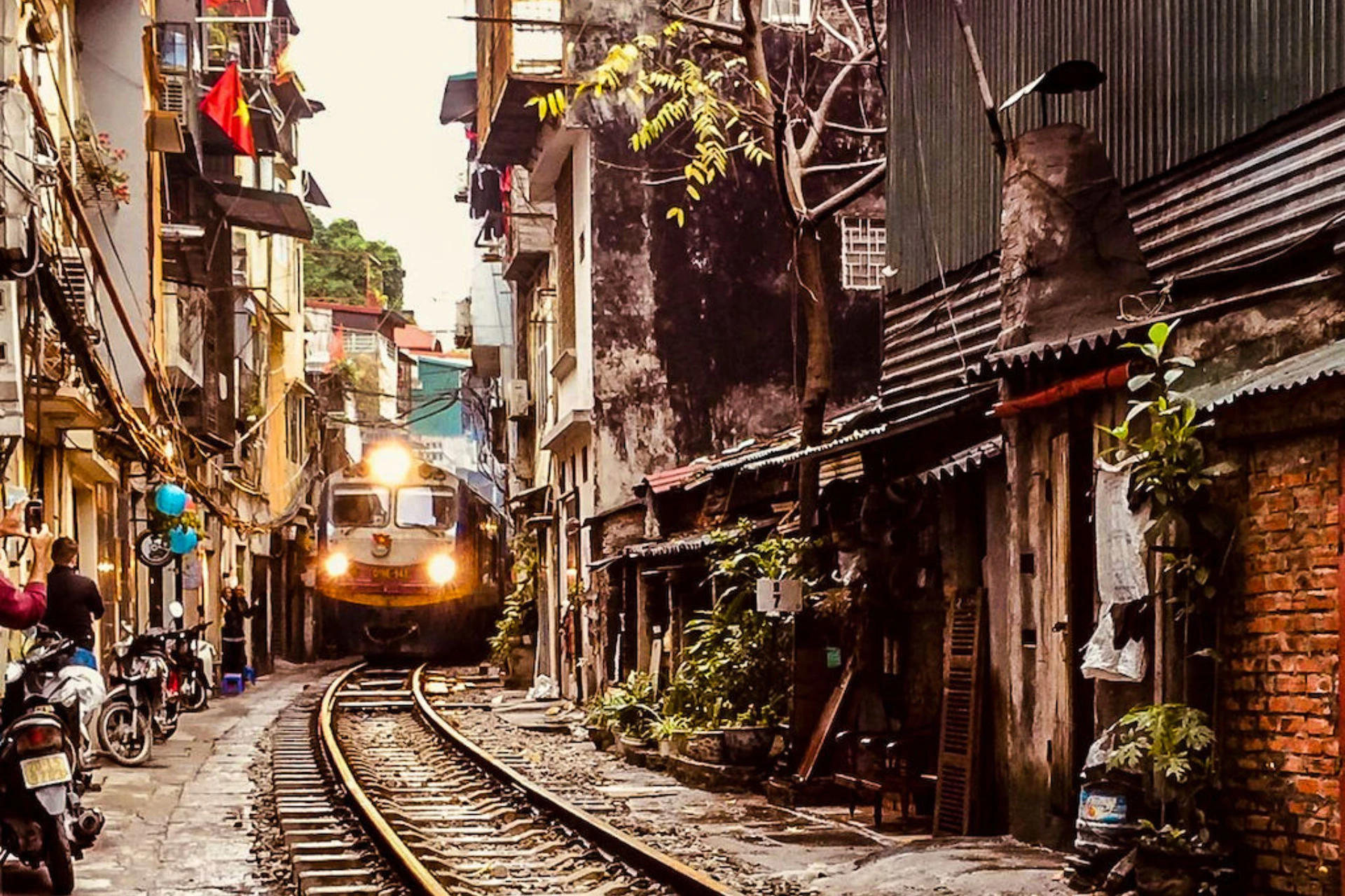 Train approaching through narrow Hanoi street with old buildings