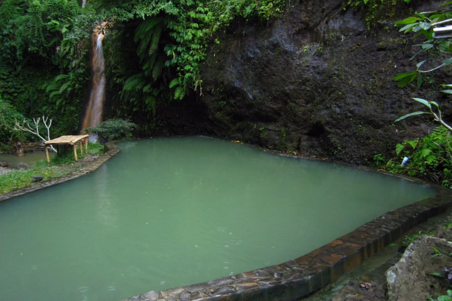 Green mineral pool with small waterfall and stone walls