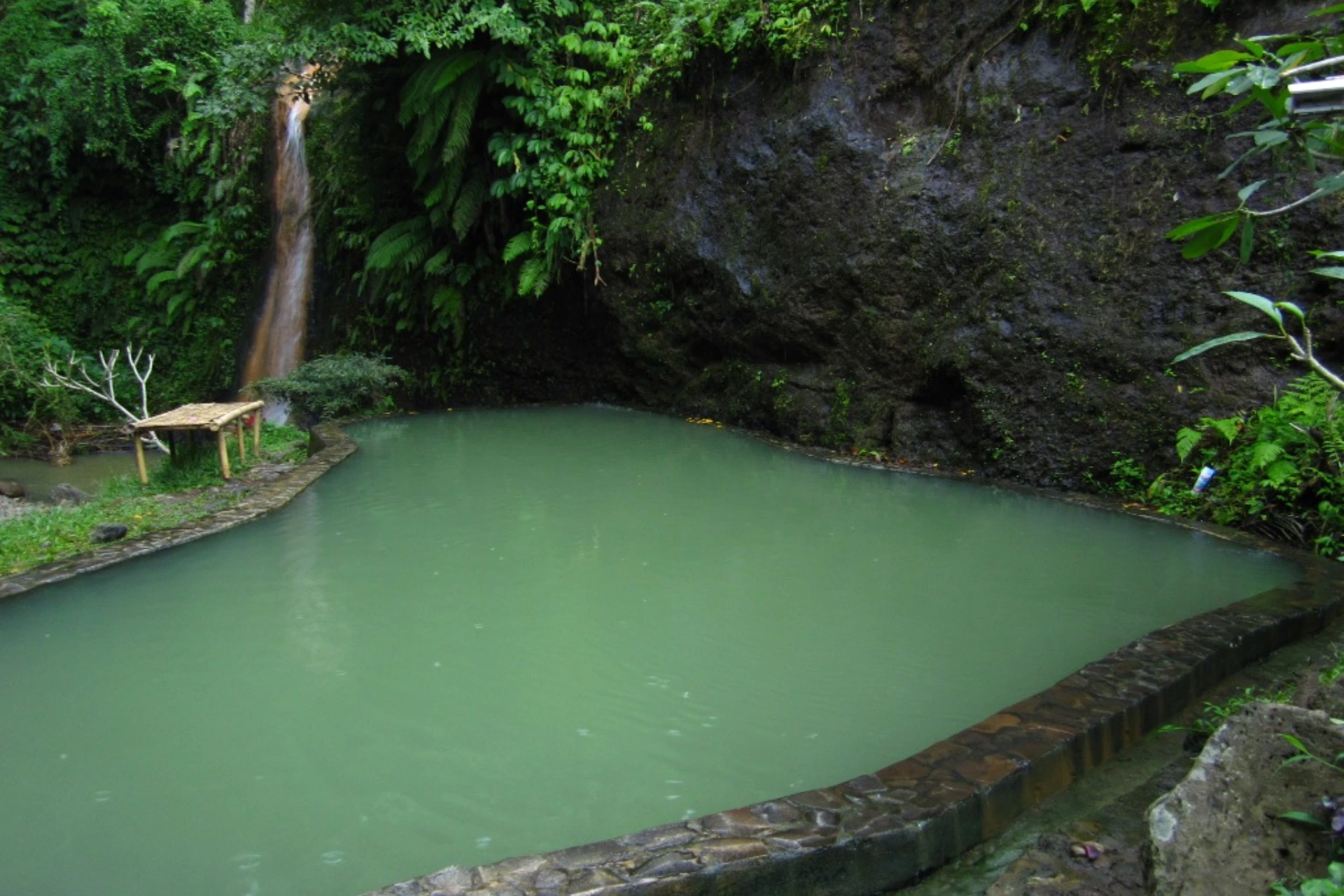 Green mineral pool with small waterfall and stone walls