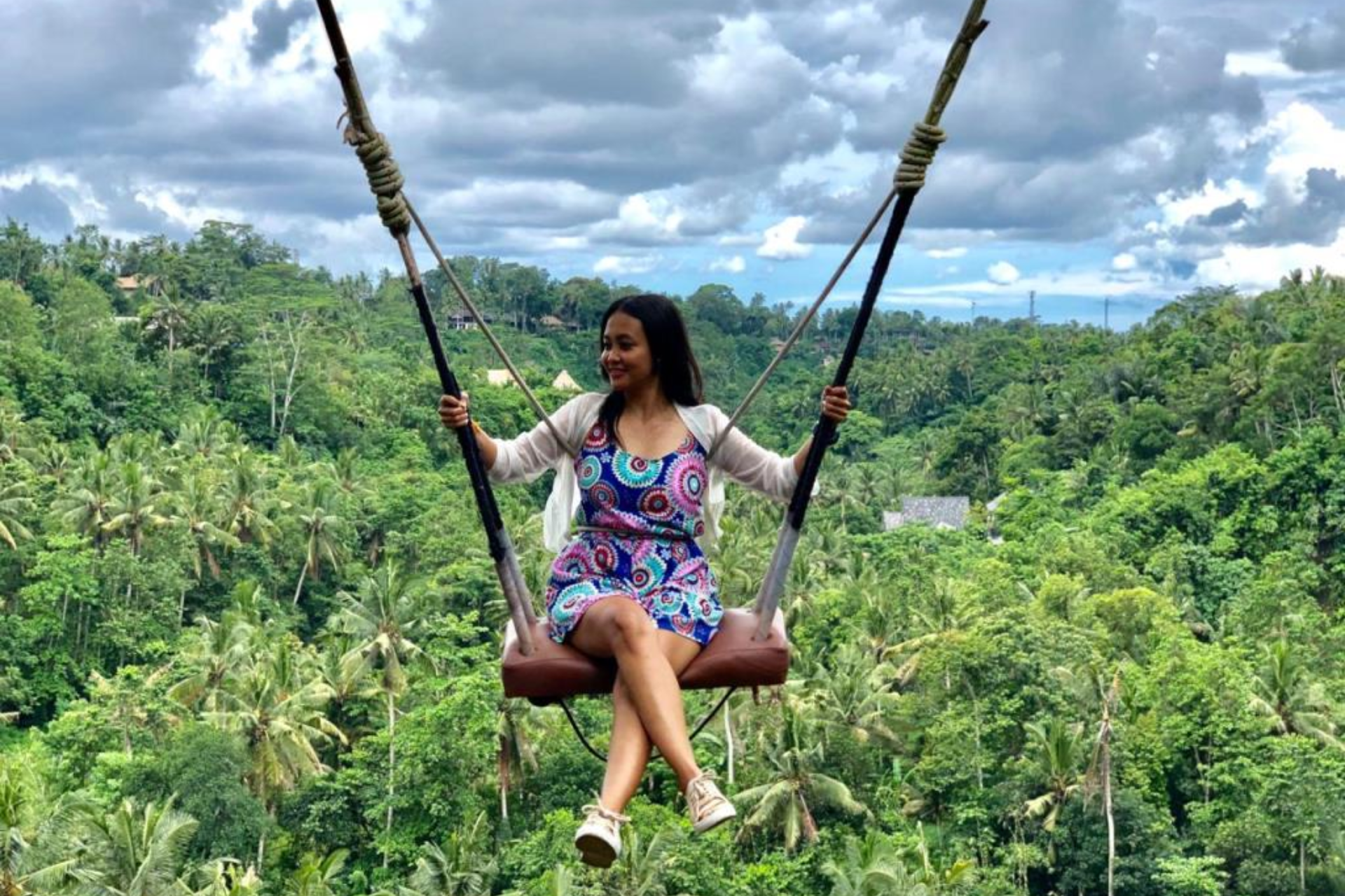 Woman on jungle swing above green forest canopy