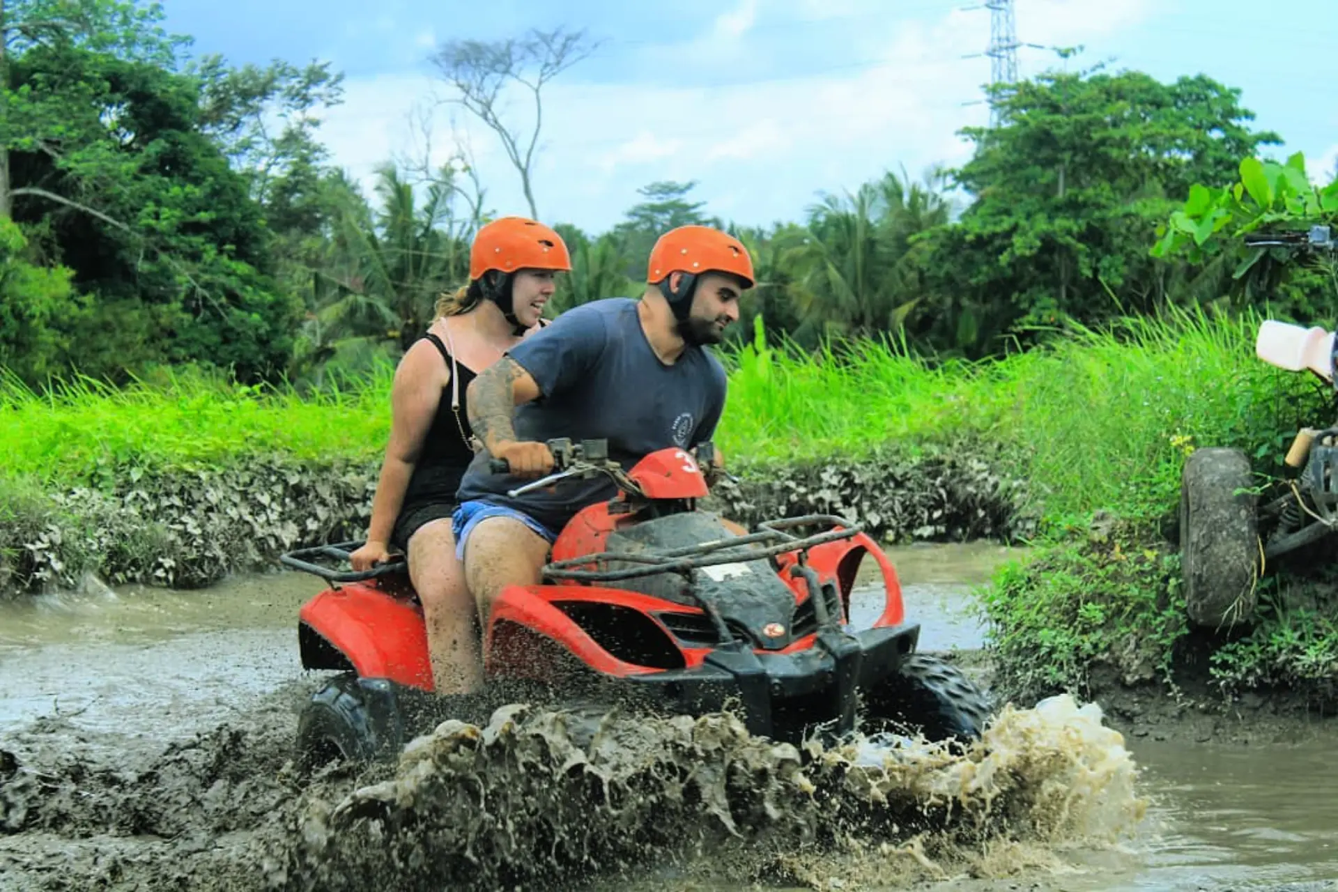 Two people riding red ATV through muddy water Bali