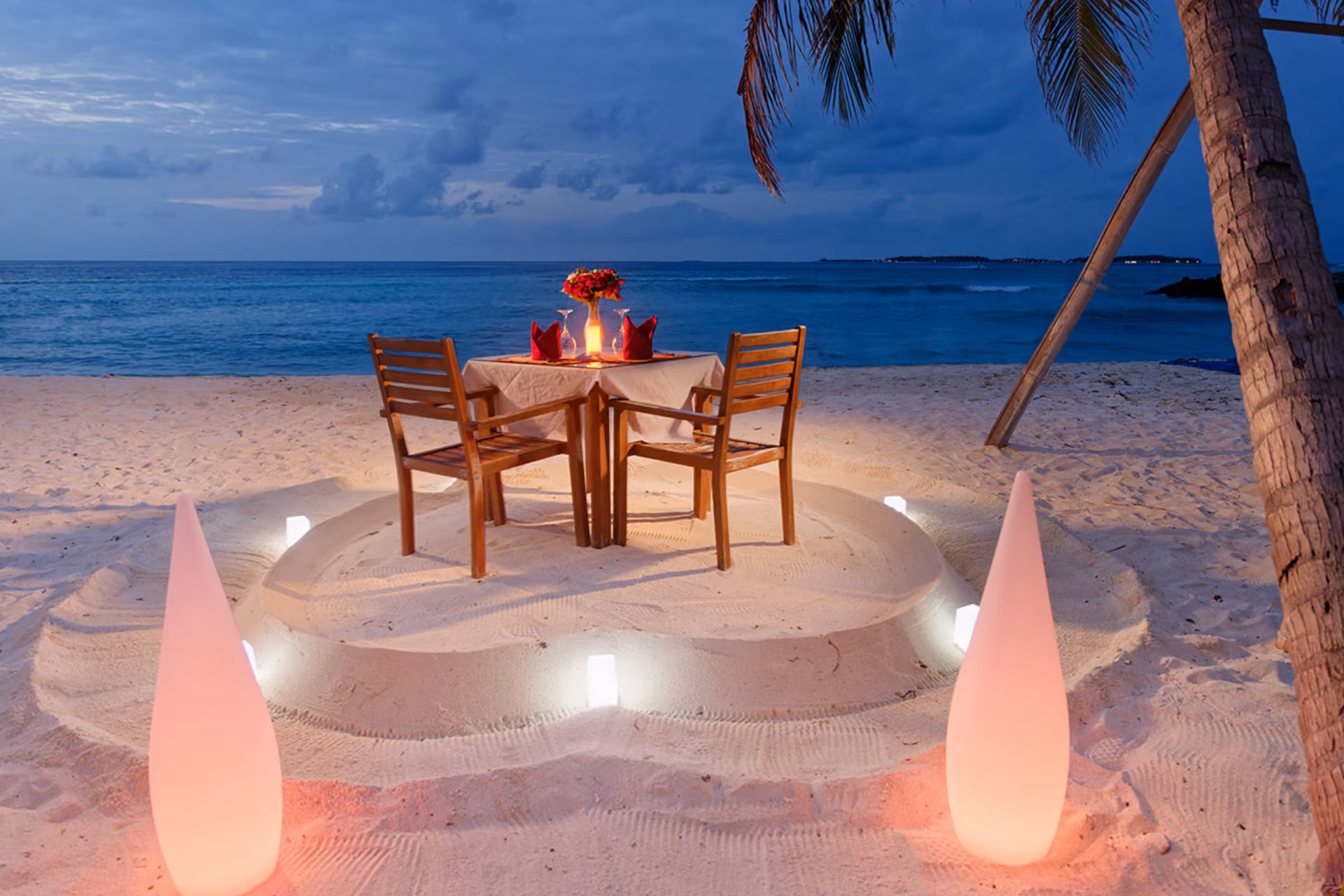 Candlelit beach dinner table by ocean at night