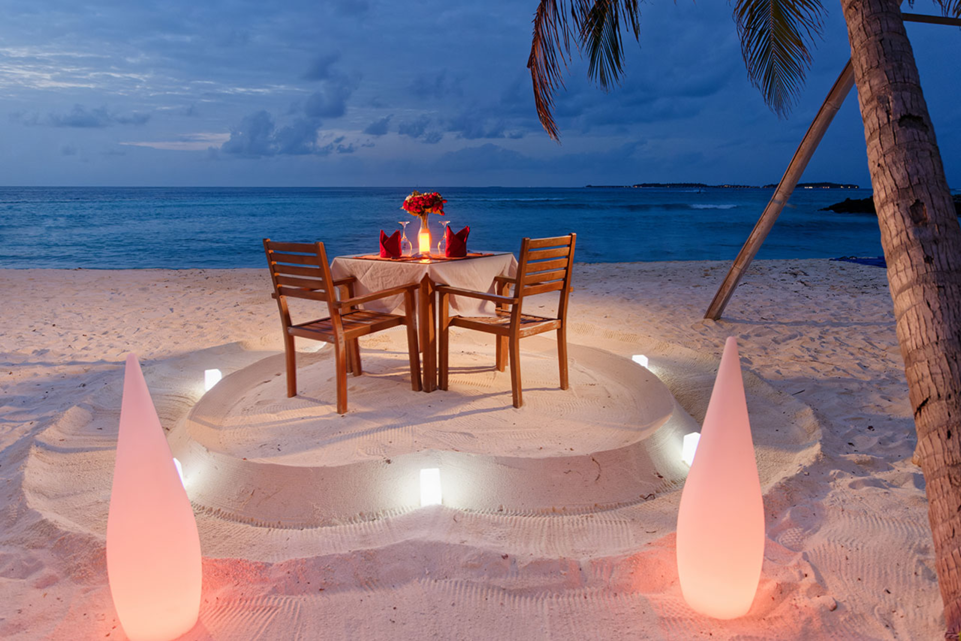 Candlelit beach dinner table by ocean at night