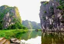 Tall rock cliffs rising above calm water at Tam Coc