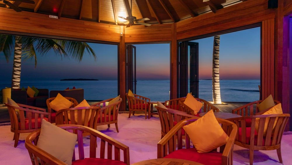Wooden chairs with orange pillows facing ocean at sunset