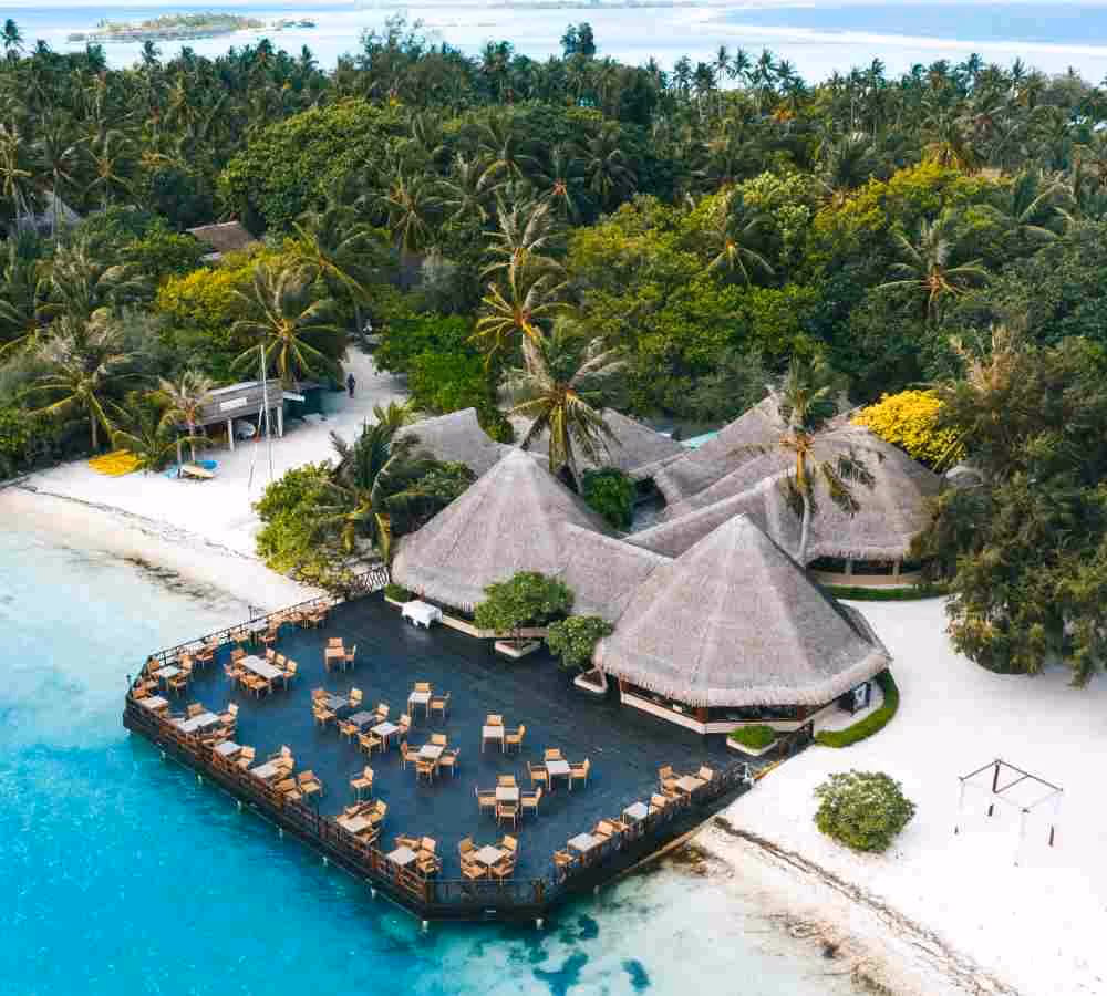 Tropical island resort with thatched-roof buildings and open-air dining deck