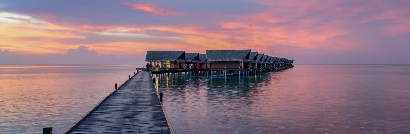 Wooden walkway leading to row of ocean villas at sunset