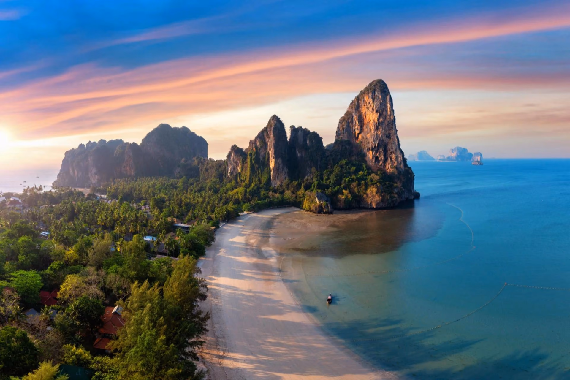A scenic tropical beach in Thailand with turquoise waters, limestone cliffs, lush greenery, and a long sandy shoreline.