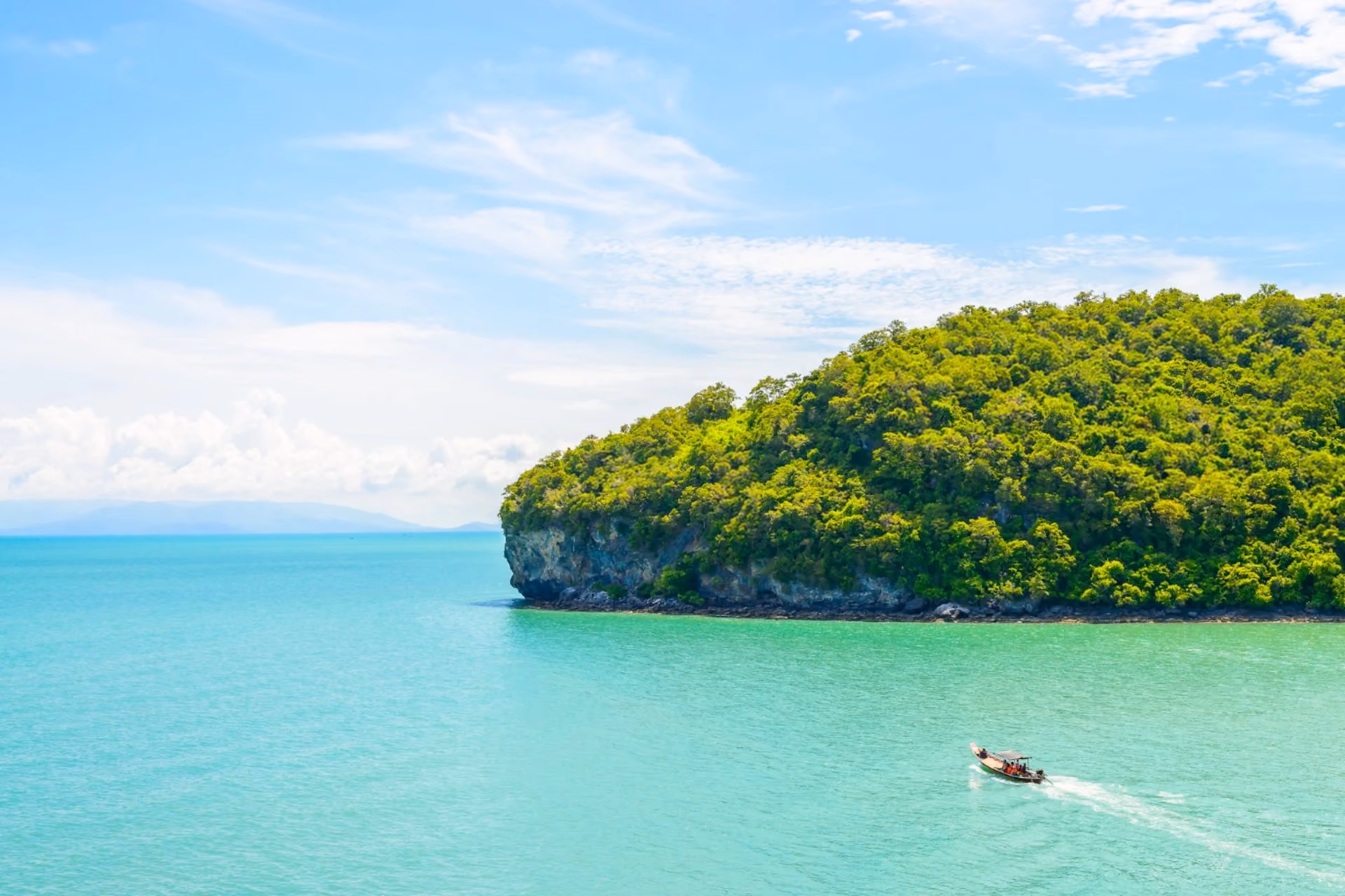 Boat cruising through the crystal-clear turquoise waters near the lush green coastline of the Perhentian Islands, Malaysia.