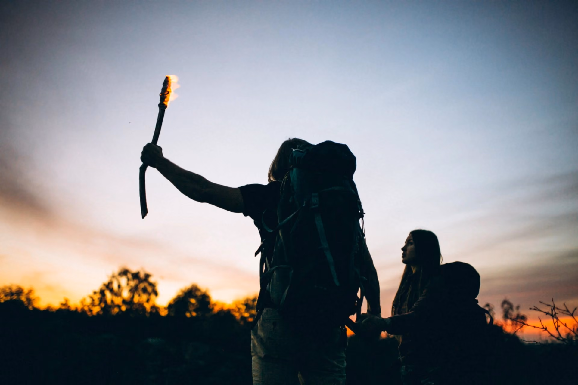 Two trekkers carrying backpacks walk at sunset, using a torch while exploring a scenic trail during a beginner-friendly trekking adventure in Vietnam.