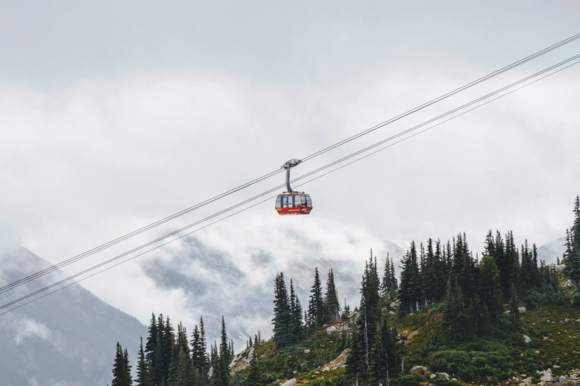 Red Kok-Tobe cable car traveling above forested hills with misty mountains in the background in Almaty, Kazakhstan.