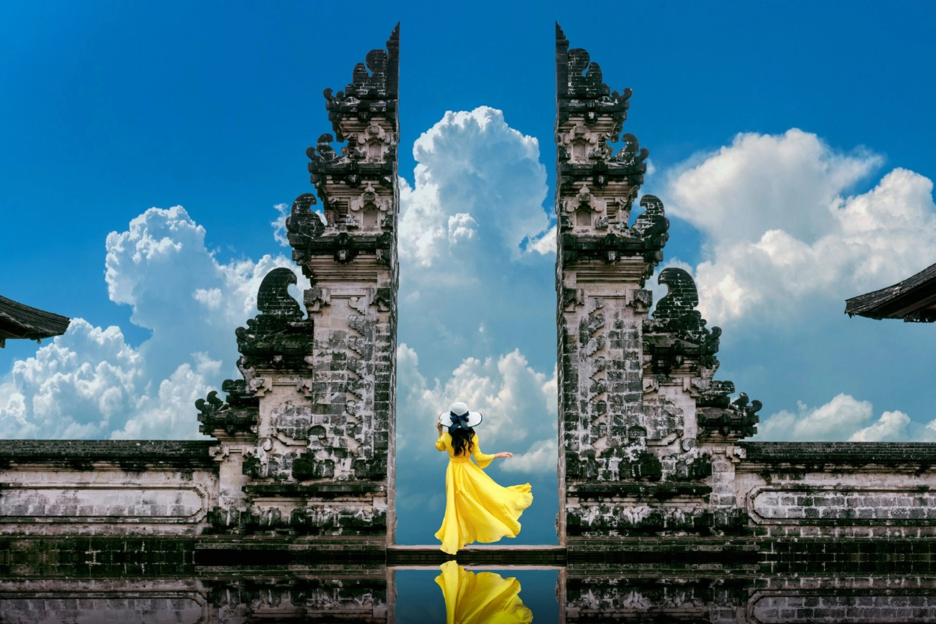 Traveller standing at Bali's iconic Heaven Gate temple with dramatic clouds, showcasing the island's tropical beauty.