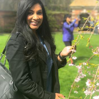 Christine Katwaru smiling outdoors near flowering spring blossoms