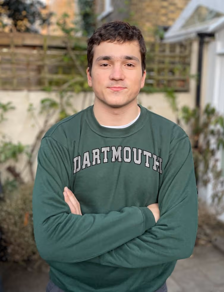Young man with arms crossed wearing a green Dartmouth sweatshirt standing outdoors.