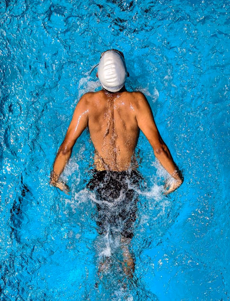 Overhead view of a swimmer wearing a white cap performing a stroke in clear blue water.