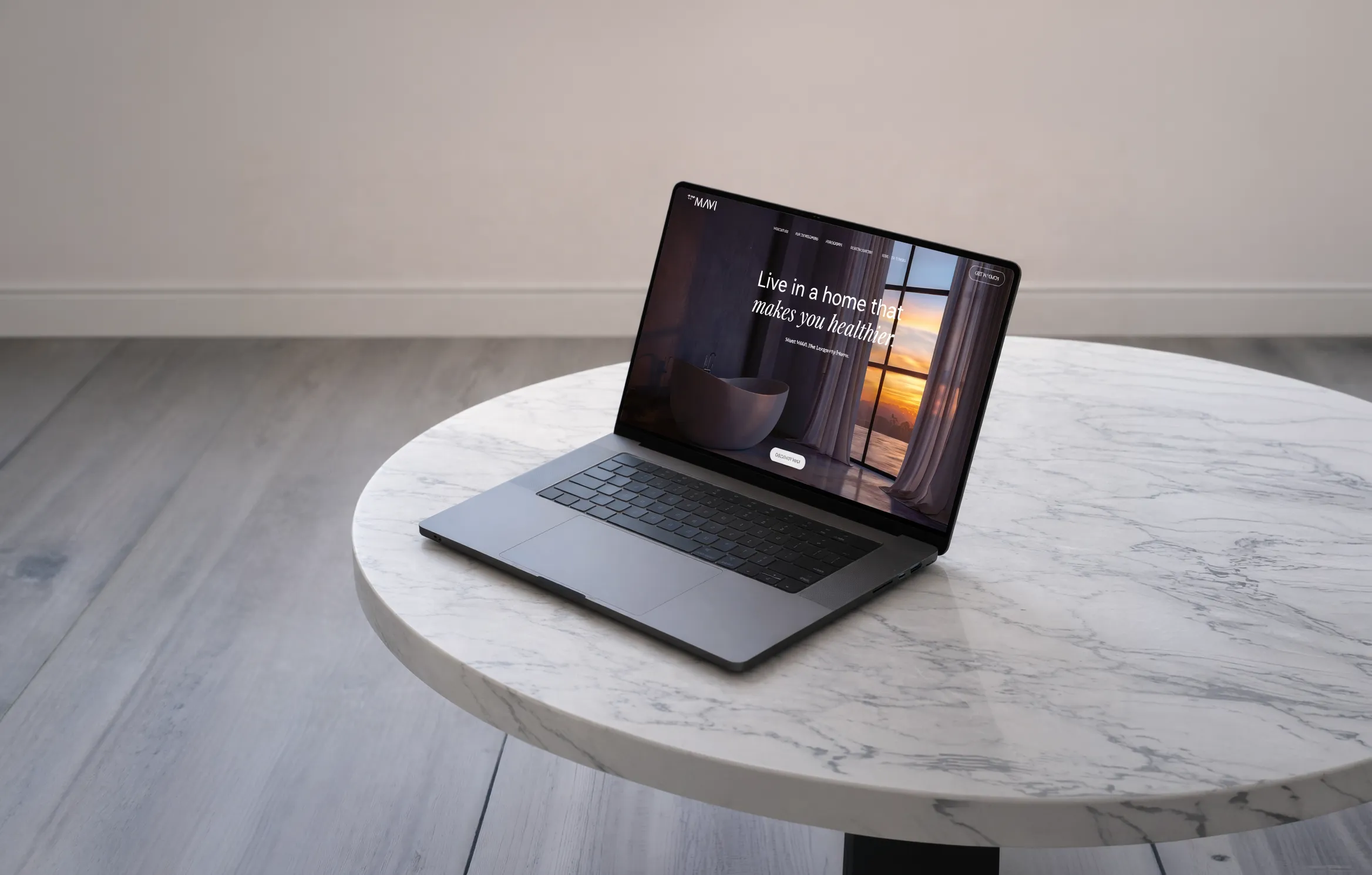Open laptop on a round white marble table displaying a website homepage with the text 'Live in a home that makes you healthier'.