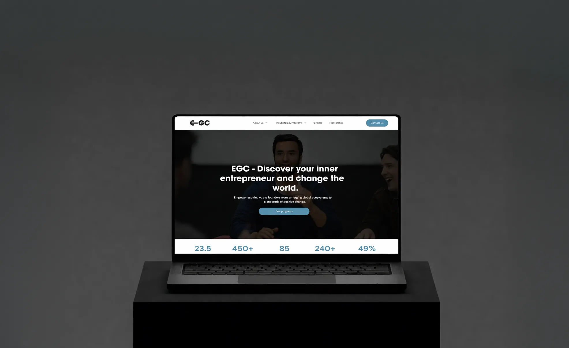 Laptop displaying EGC website homepage with the text 'Discover your inner entrepreneur and change the world' and a button labeled 'See programs'.