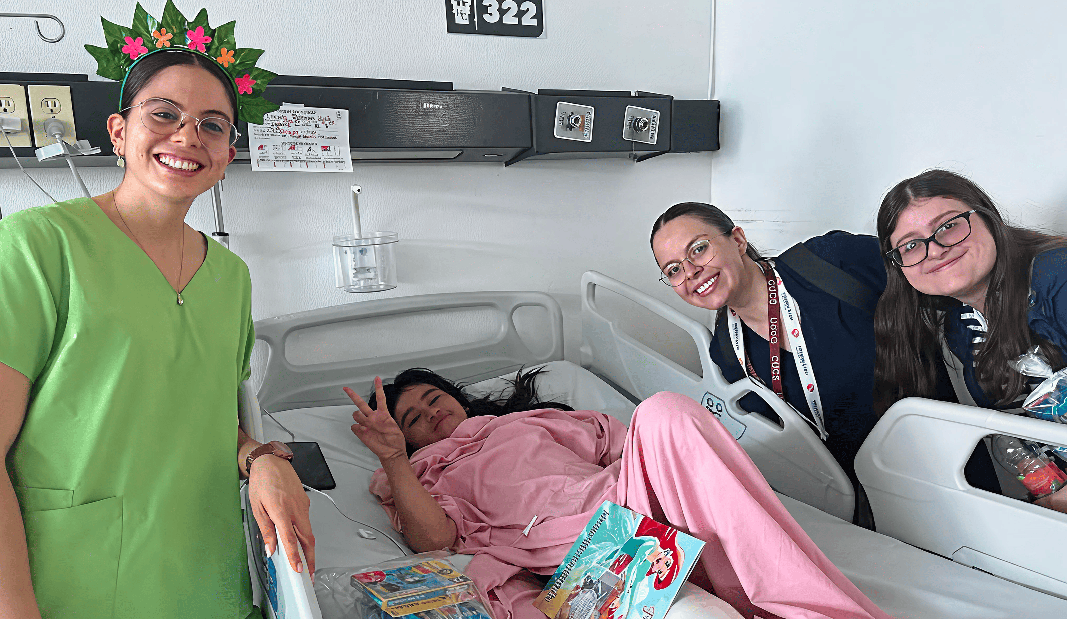 A patient in pink flashes a peace sign while smiling with three Mission:Brain volunteers by her bedside—capturing a lighthearted, uplifting moment during the Guadalajara mission.