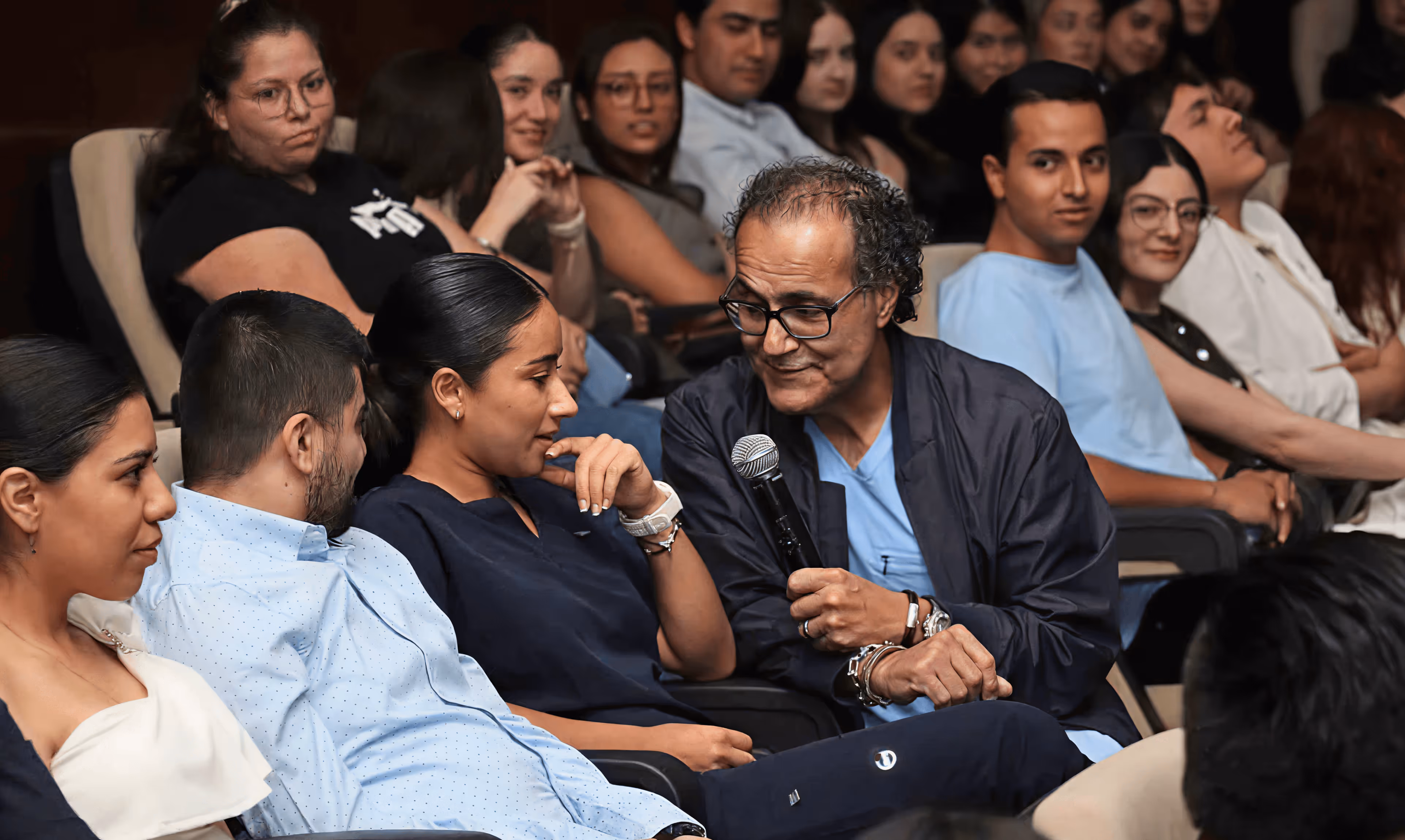 A young patient smiles in bed while proudly showing her drawing, joined by two Mission:Brain volunteers—capturing a joyful moment of connection and creativity during the Guadalajara outreach.