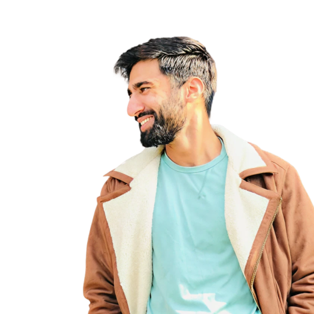 Man with short dark hair and a full beard, wearing a light blue t-shirt and a brown jacket with a white fleece lining, smiling and looking to his left.