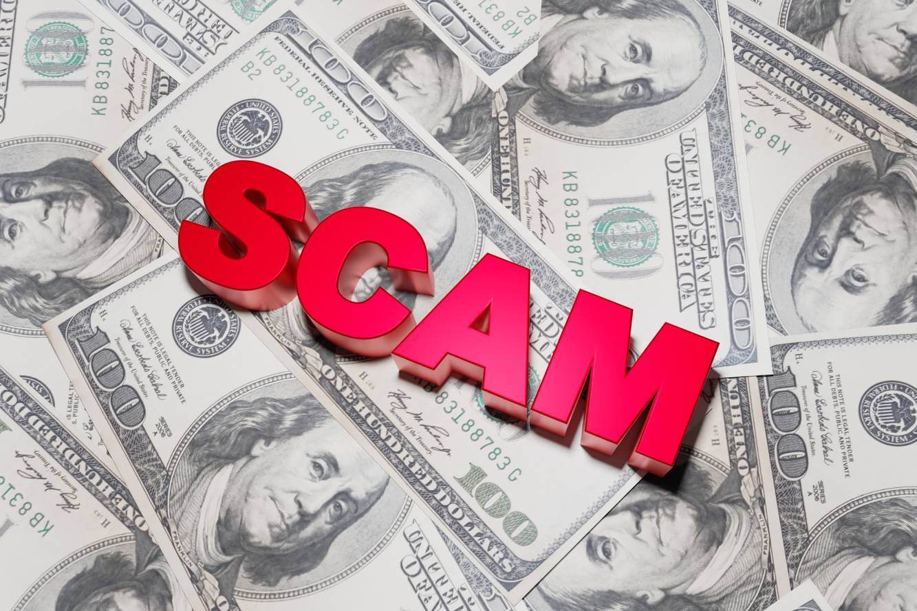 the word scam written in red letters and paper $100 bills to symbolize a cryptocurrency scam