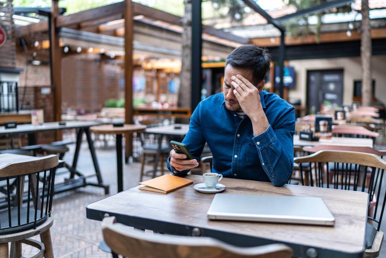 businessman on a coffee break looking a possible application-to-person fraud on his phone text messages