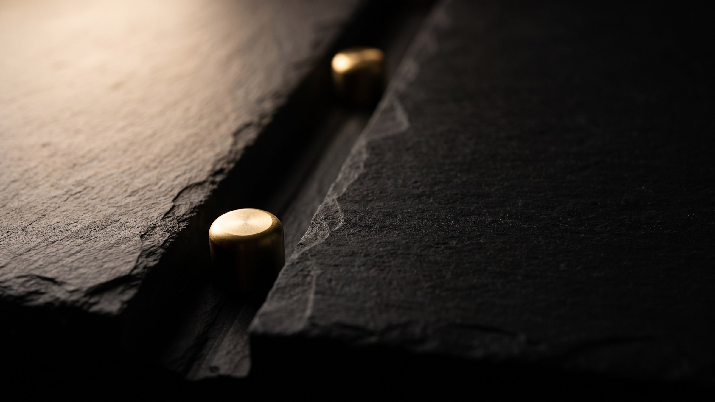 Two small brass markers set at different points along a channel cut into dark stone, lit by a single warm light