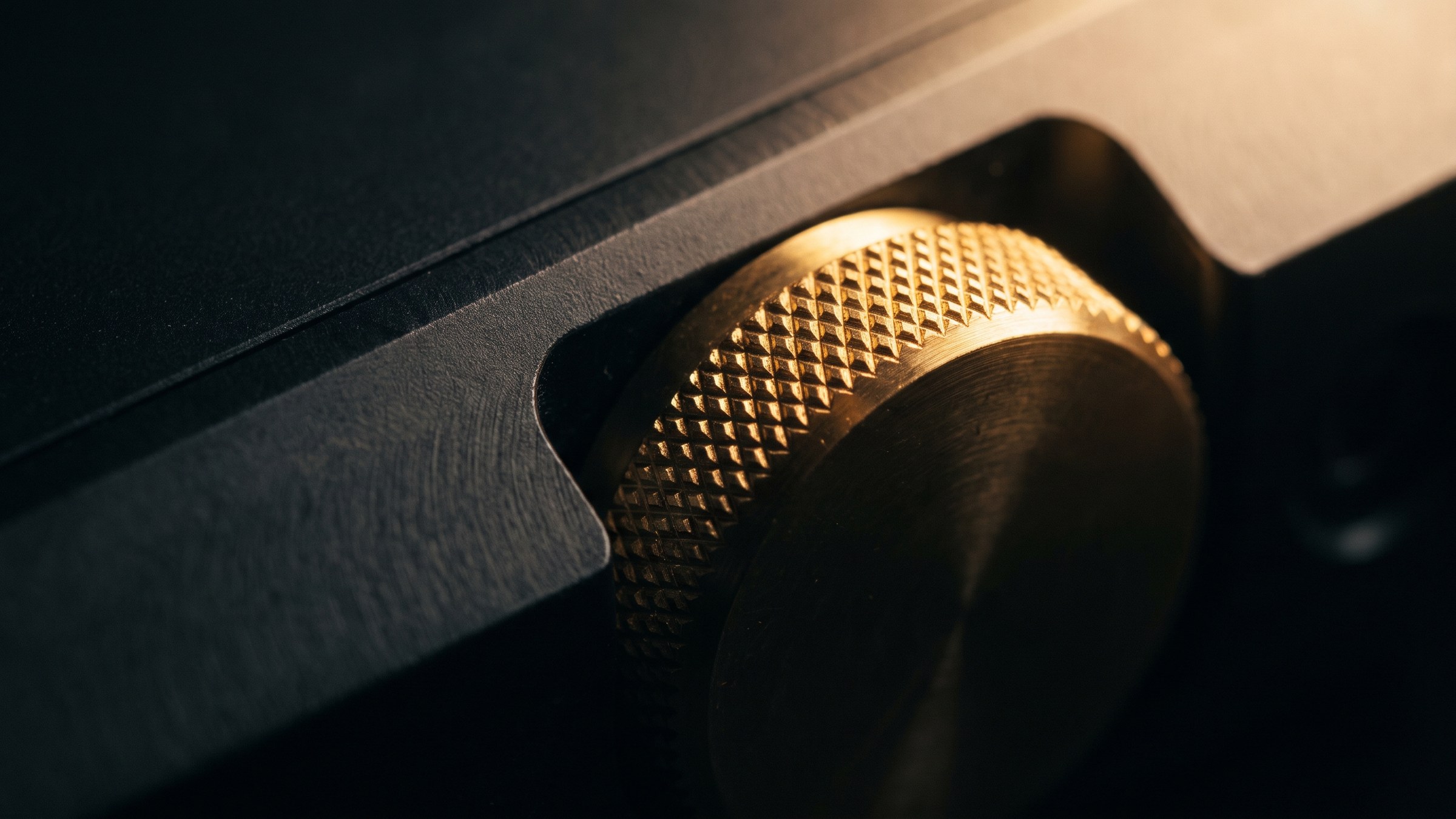 A knurled brass adjustment dial set into a dark machined panel, lit from the upper right