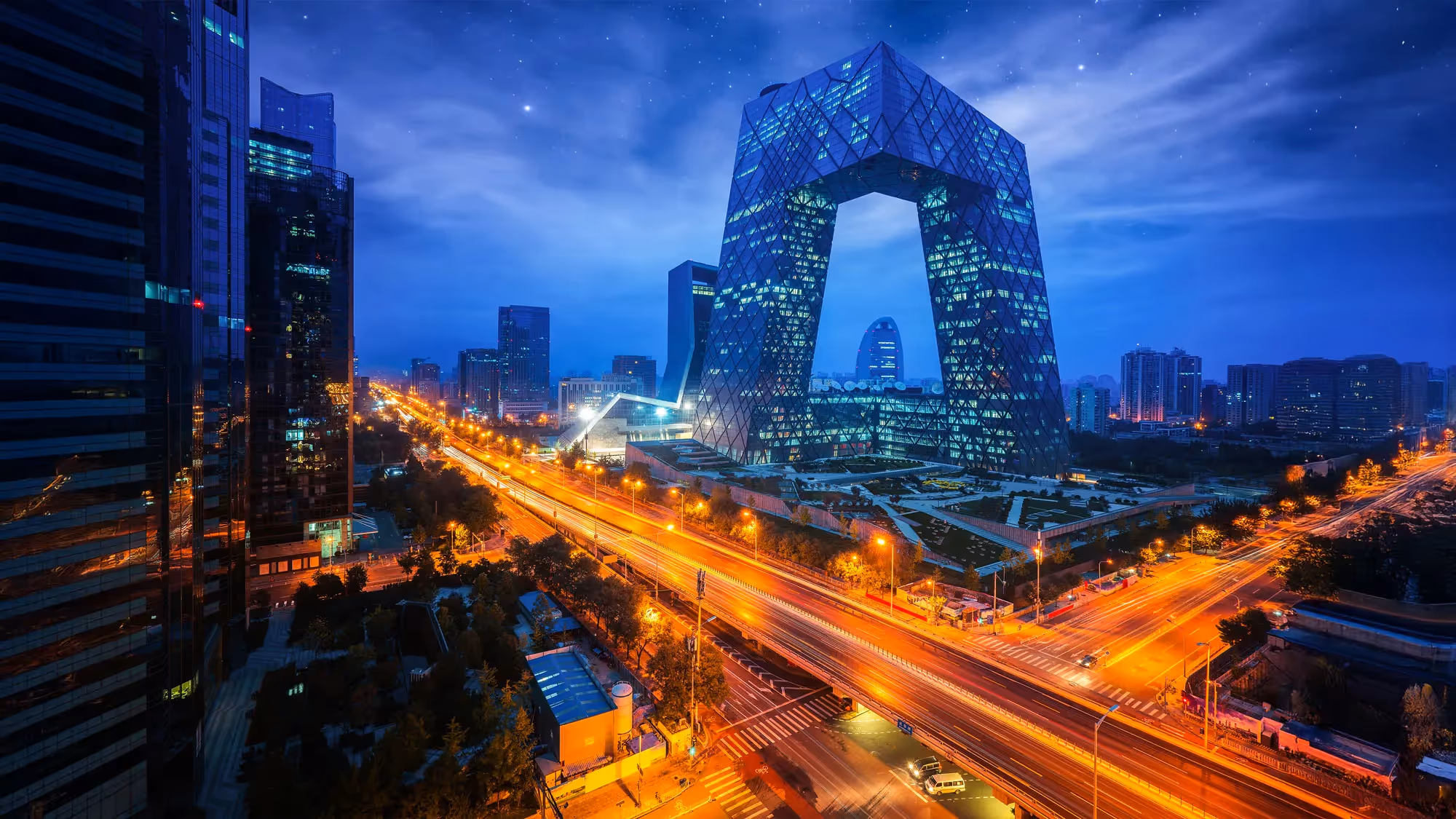 Cityscape of Beijing, China, featuring the illuminated CCTV Headquarters at night with modern buildings and busy streets showcasing vibrant city life.