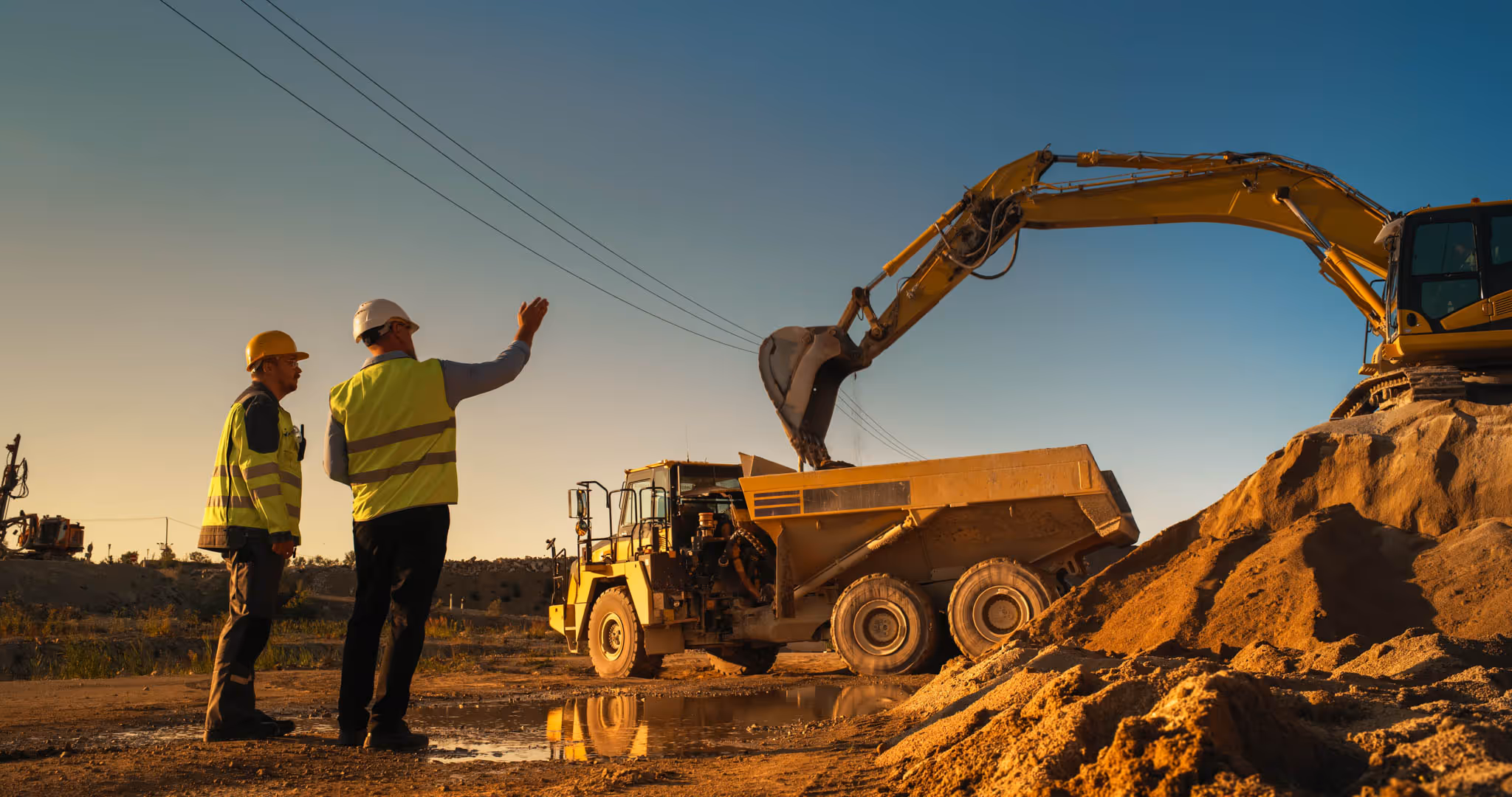 Two construction workers looking up at a digger, digging up earth.