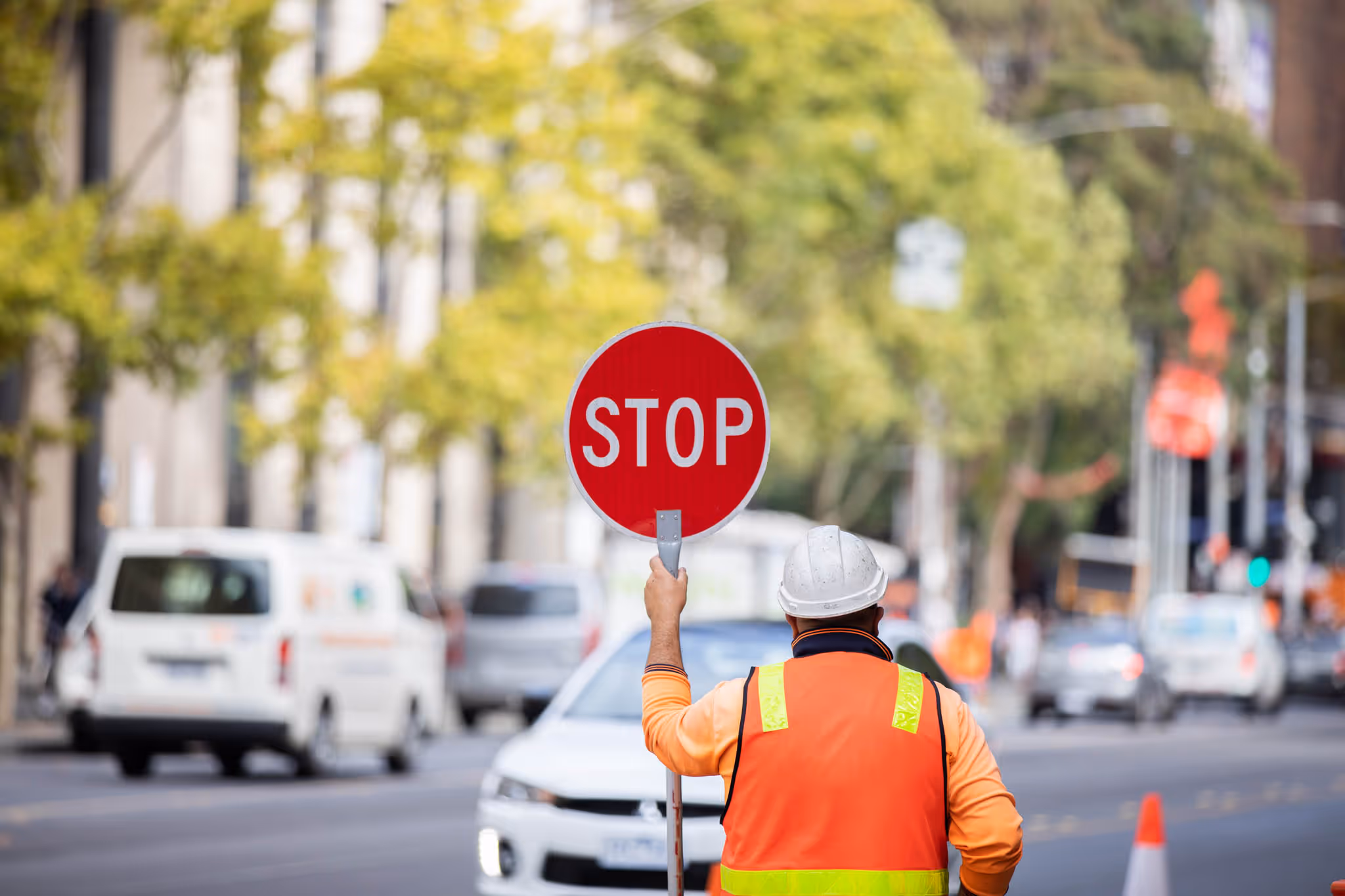 Construction worker holding up a stop sign in front of traffic on a busy road.
