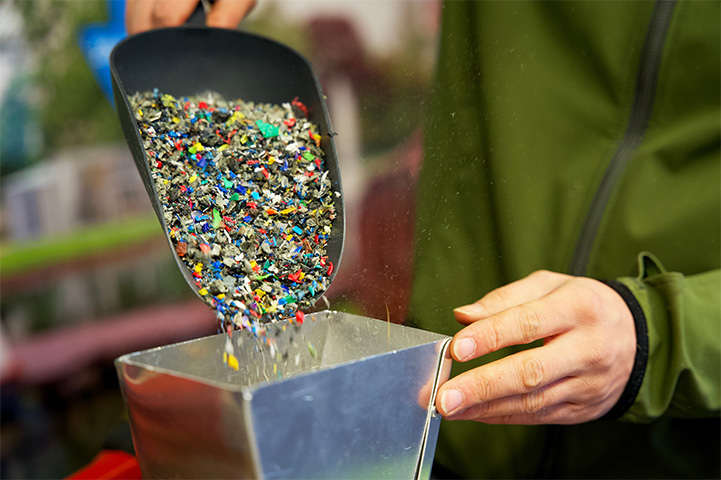 Person pouring recycled materials from a scoop into a container.