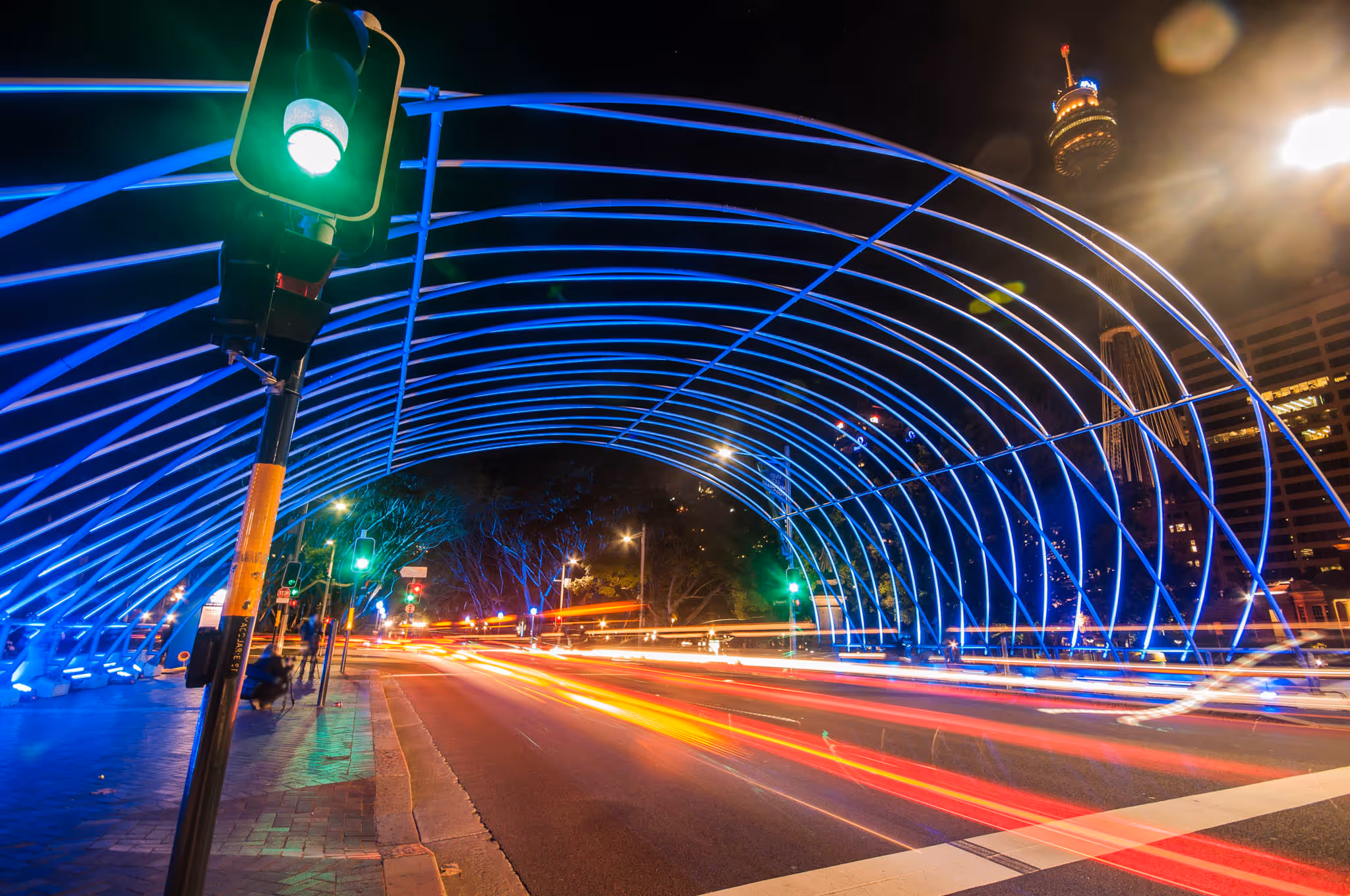 Green traffic lights along a road at night with cars driving by.