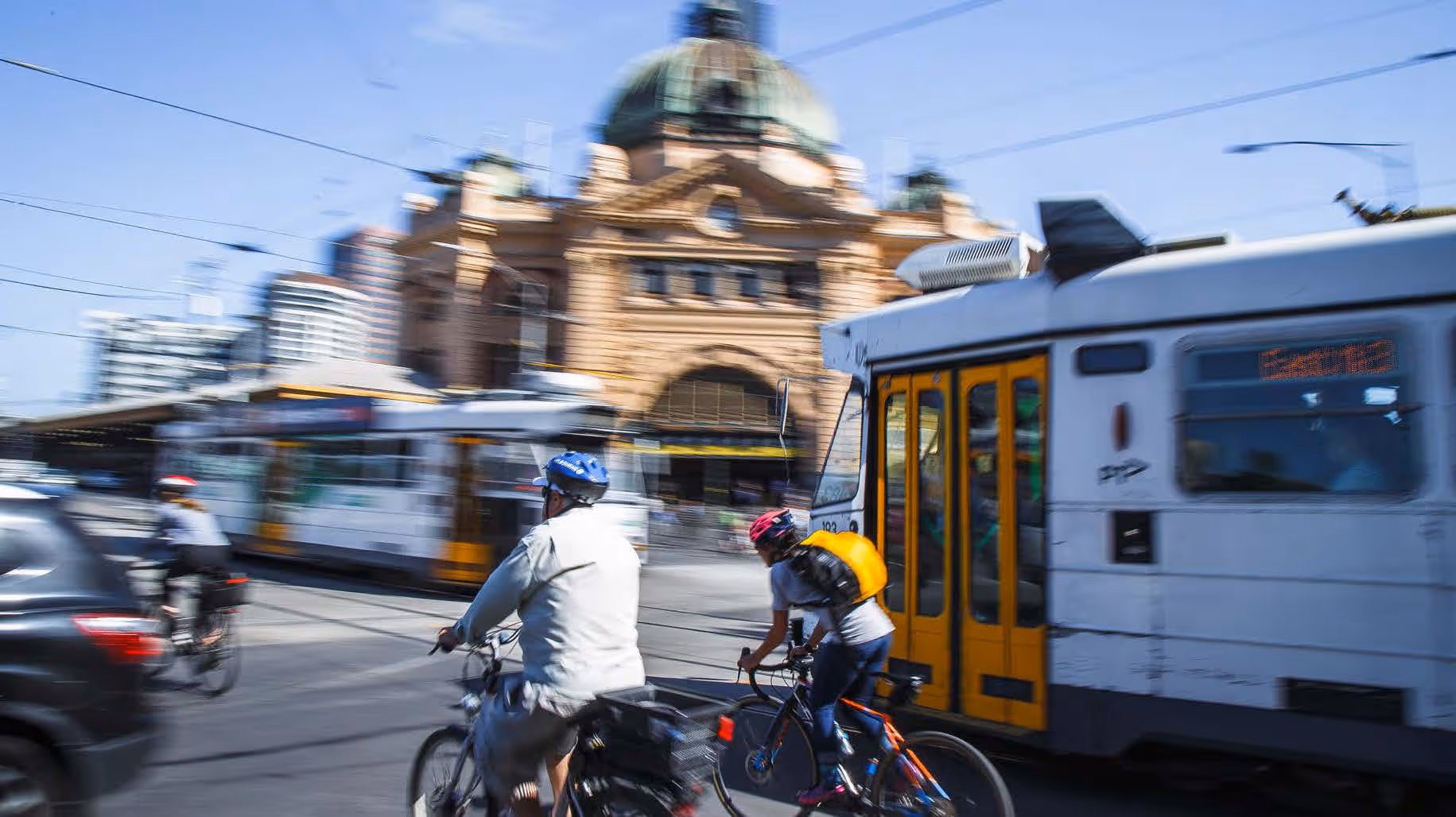 Cyclists riding in front of moving Melbourne trams.