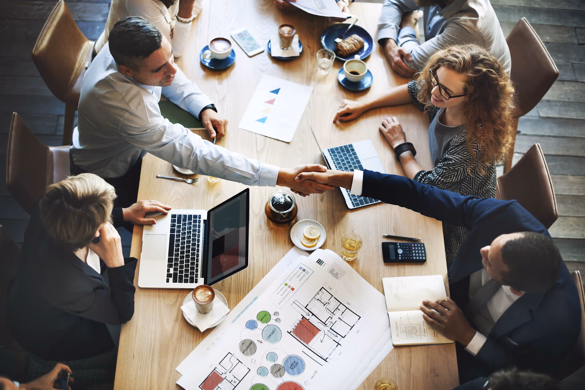 People sat around a meeting room desk shaking hands.